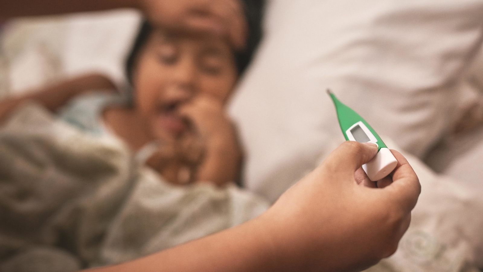 La mère d'une enfant couchée dans un lit prend sa température à l'aide d'un thermomètre.