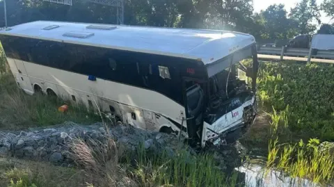 Virginia State Police A white and black bus sits on greenery on the side of a road after a crash.